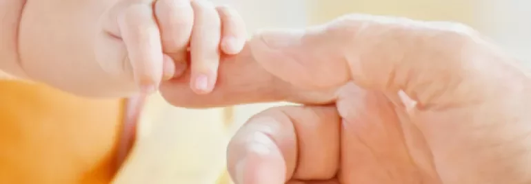 Baby hand holding an adult's finger gently.