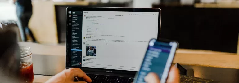 Persoon werkt op laptop en smartphone in een café.
