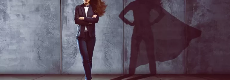 Person in suit stands with superhero shadow on wall.