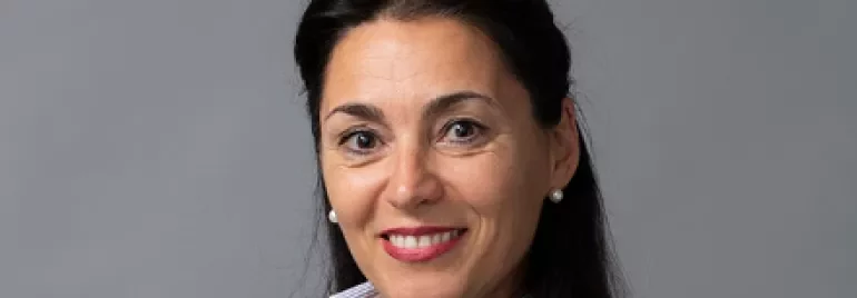 A smiling person in a dark jacket against a gray background.