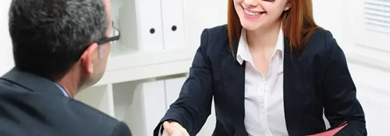 Two people shaking hands at a desk during a meeting.