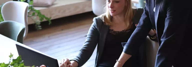 Two people collaborating on a laptop at a desk.