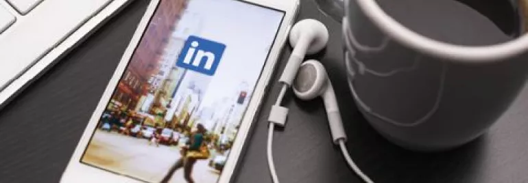 Smartphone displaying LinkedIn app beside a cup of coffee and keyboard.