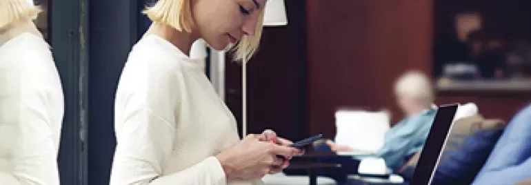 Person using a smartphone while seated with a laptop nearby.