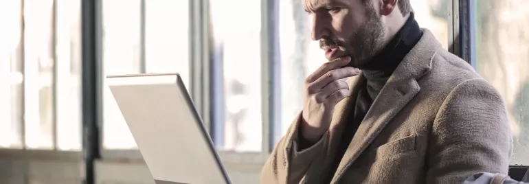 Persoon kijkt aandachtig naar laptop bij raam.