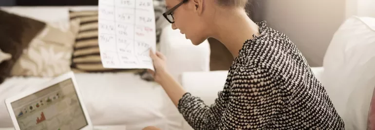 Person examining a document while working on a laptop.