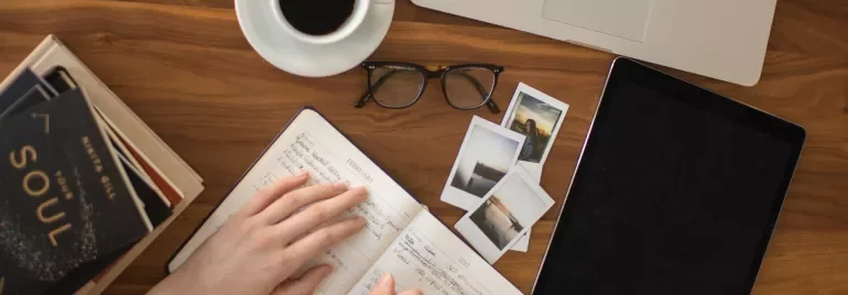 Person writing in notebook with laptop and coffee on table.