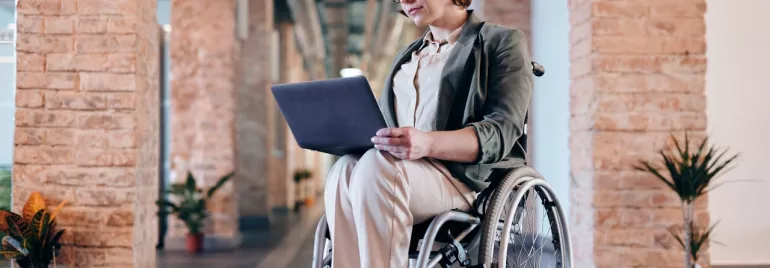 Persoon met een laptop in een rolstoel in een ruime gang.