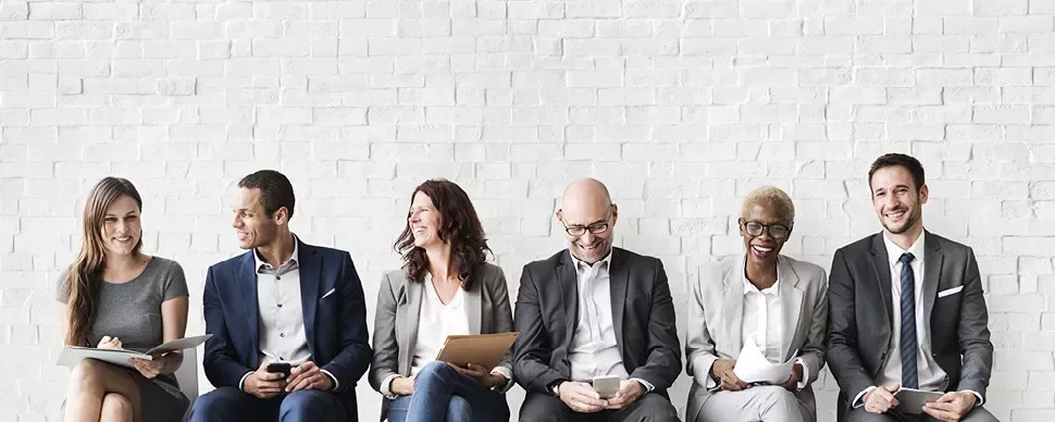 A group of people in business attire sitting against a brick wall.
