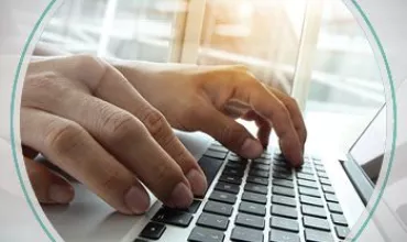 Handen typen op een laptoptoetsenbord bij een raam.