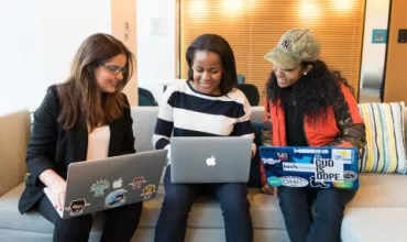 Drie mensen zitten op een bank met laptops en kijken naar het scherm.