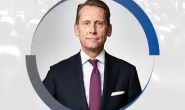 Portrait of a person in a suit with a purple tie, background with blue and grey circles.