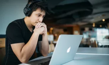 Persoon met koptelefoon kijkt aandachtig naar een laptop.