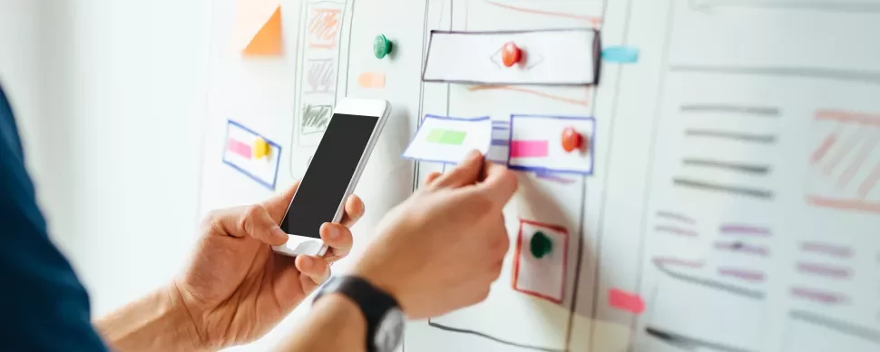 Iemand plaatst een briefje op een whiteboard met een smartphone in de hand.