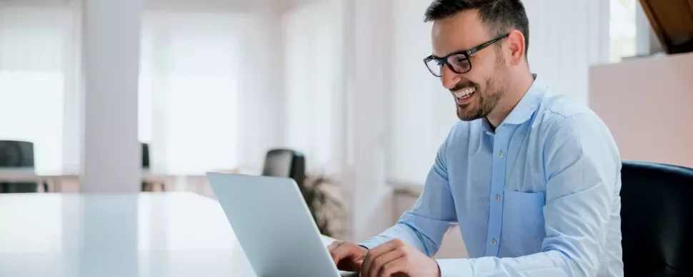 Persoon die lacht terwijl hij op een laptop typt in een kantooromgeving