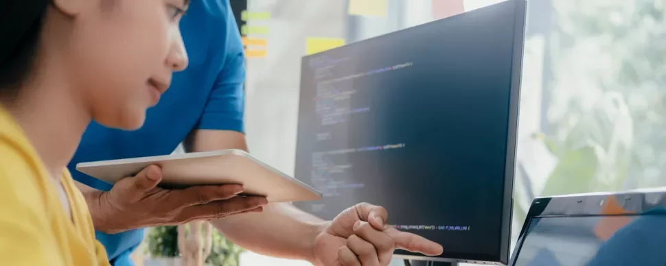 Twee mensen werken op een computer, één wijst naar het scherm.