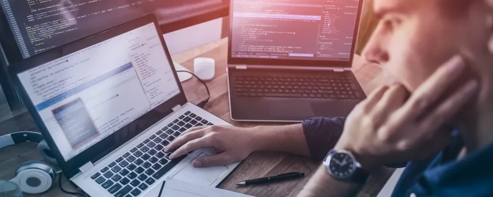 Persoon werkt aan computercode op laptops.
