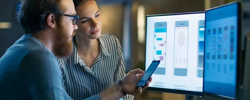 Twee personen werken aan mobiele app-ontwerp op een computerscherm.