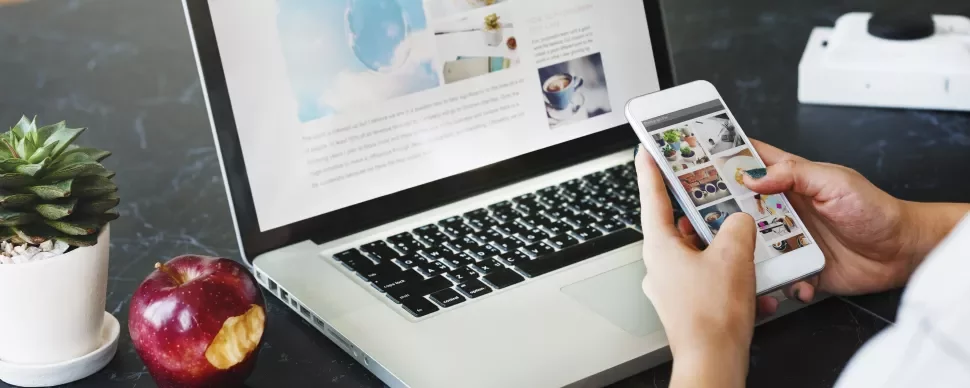 Iemand gebruikt een smartphone met een laptop op tafel.