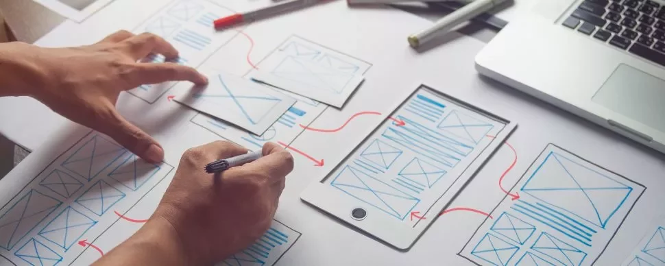Ontwerper werkt aan mobiel ontwerp met wireframes en laptop.