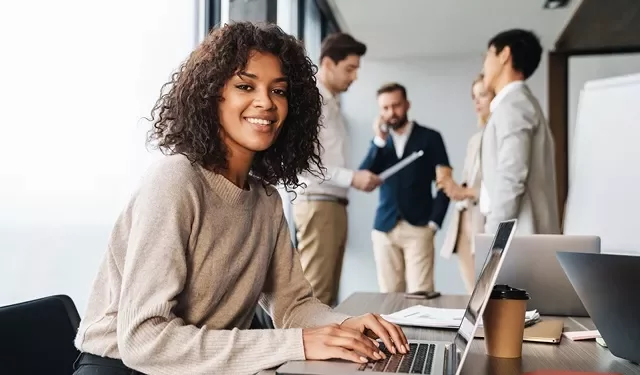Group of people in an office, one person smiling at a laptop.