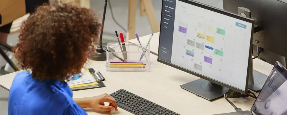 Persoon werkt aan bureau met computerscherm en agenda.