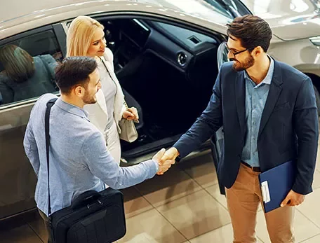 Drie mensen staan bij een auto en schudden elkaar de hand in een showroom.
