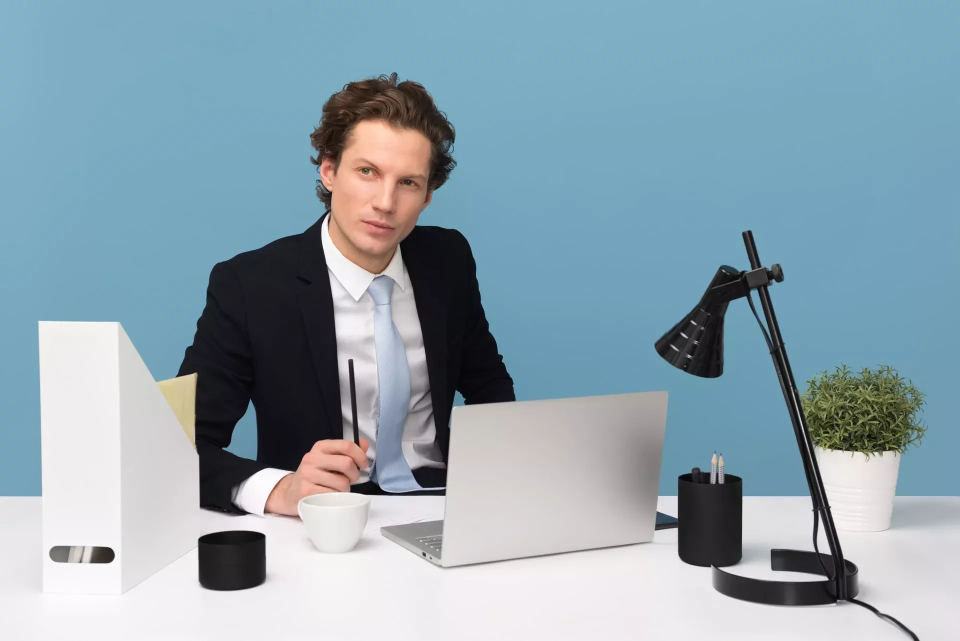 Persoon achter bureau met laptop en notitieblok, blauwe achtergrond.
