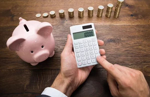 Person using a calculator near a piggy bank and stacks of coins.