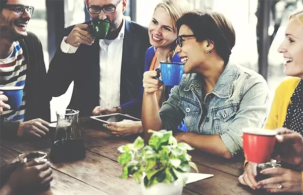 Group of people having coffee together and smiling around a table.