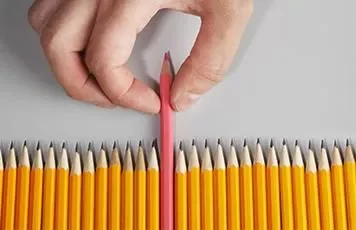 Hand picking a pink pencil from a line of yellow pencils.