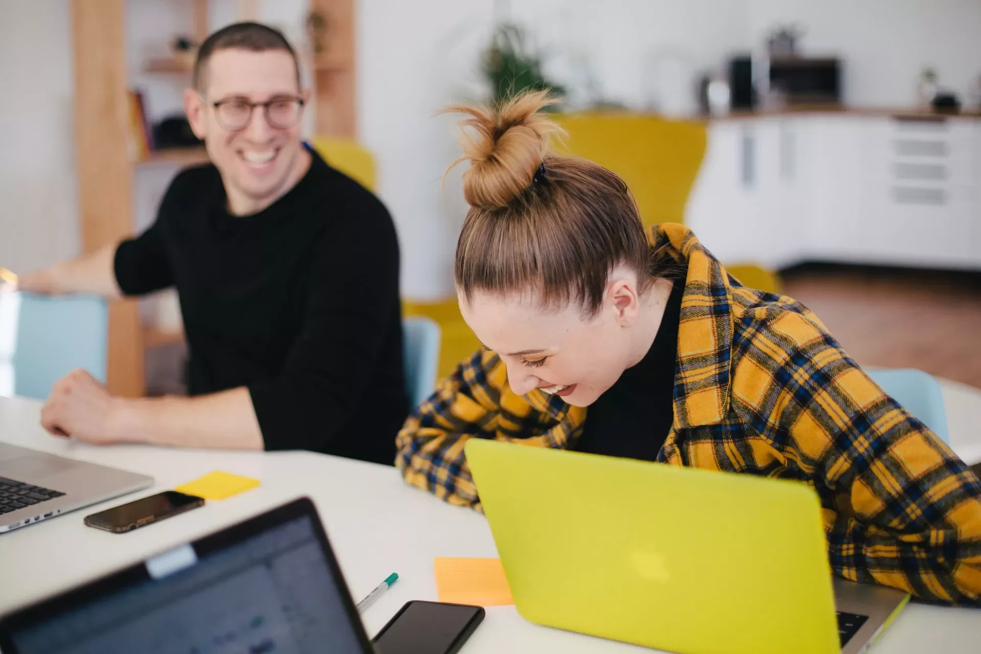 Two people laughing together while working on laptops.