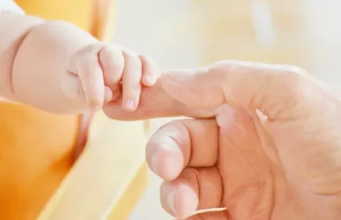 Baby hand holding an adult's finger gently.