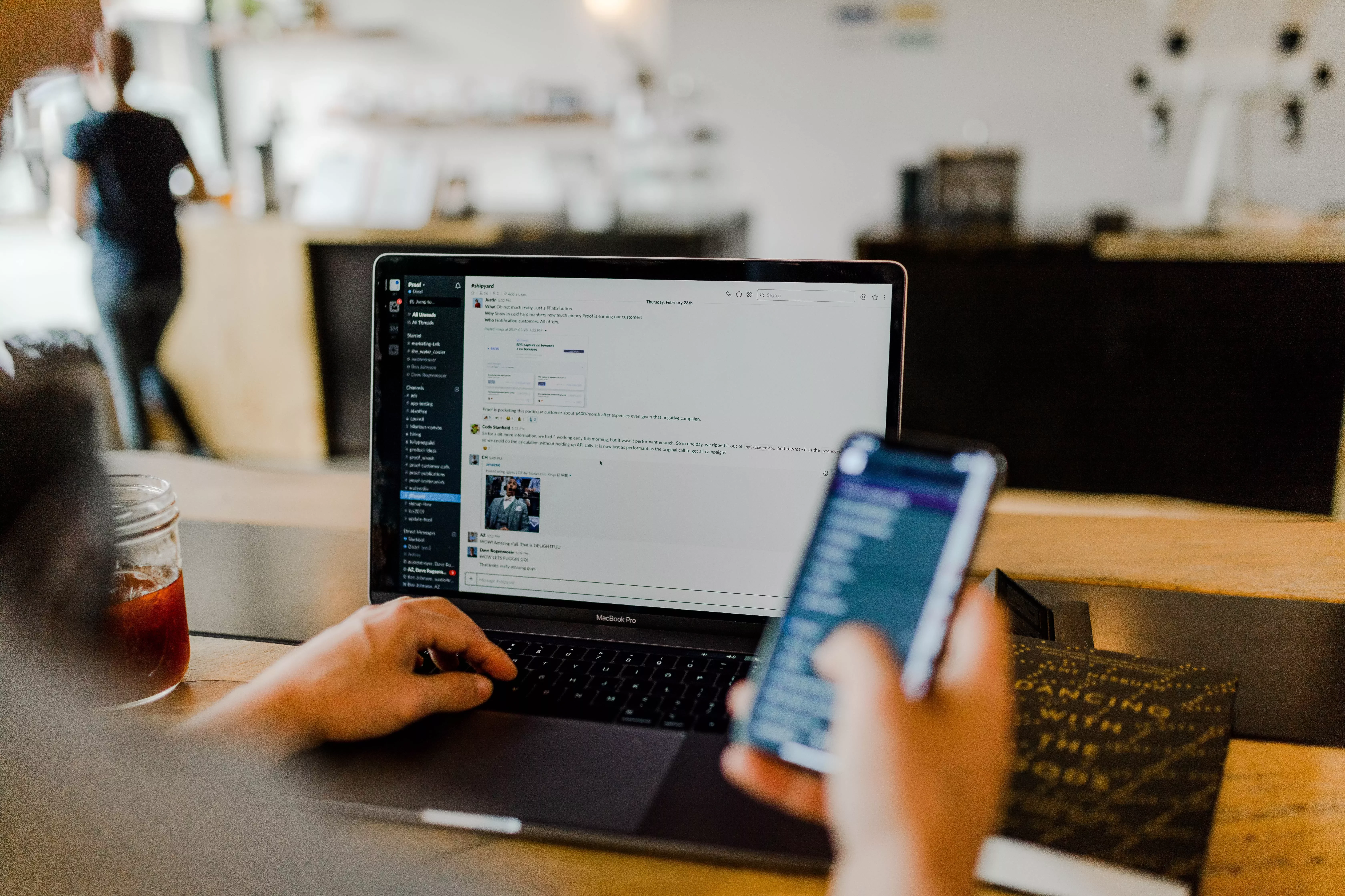 Persoon werkt op laptop en smartphone in een café.