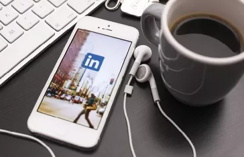 Een smartphone met de LinkedIn-app, naast een kop koffie en toetsenbord.