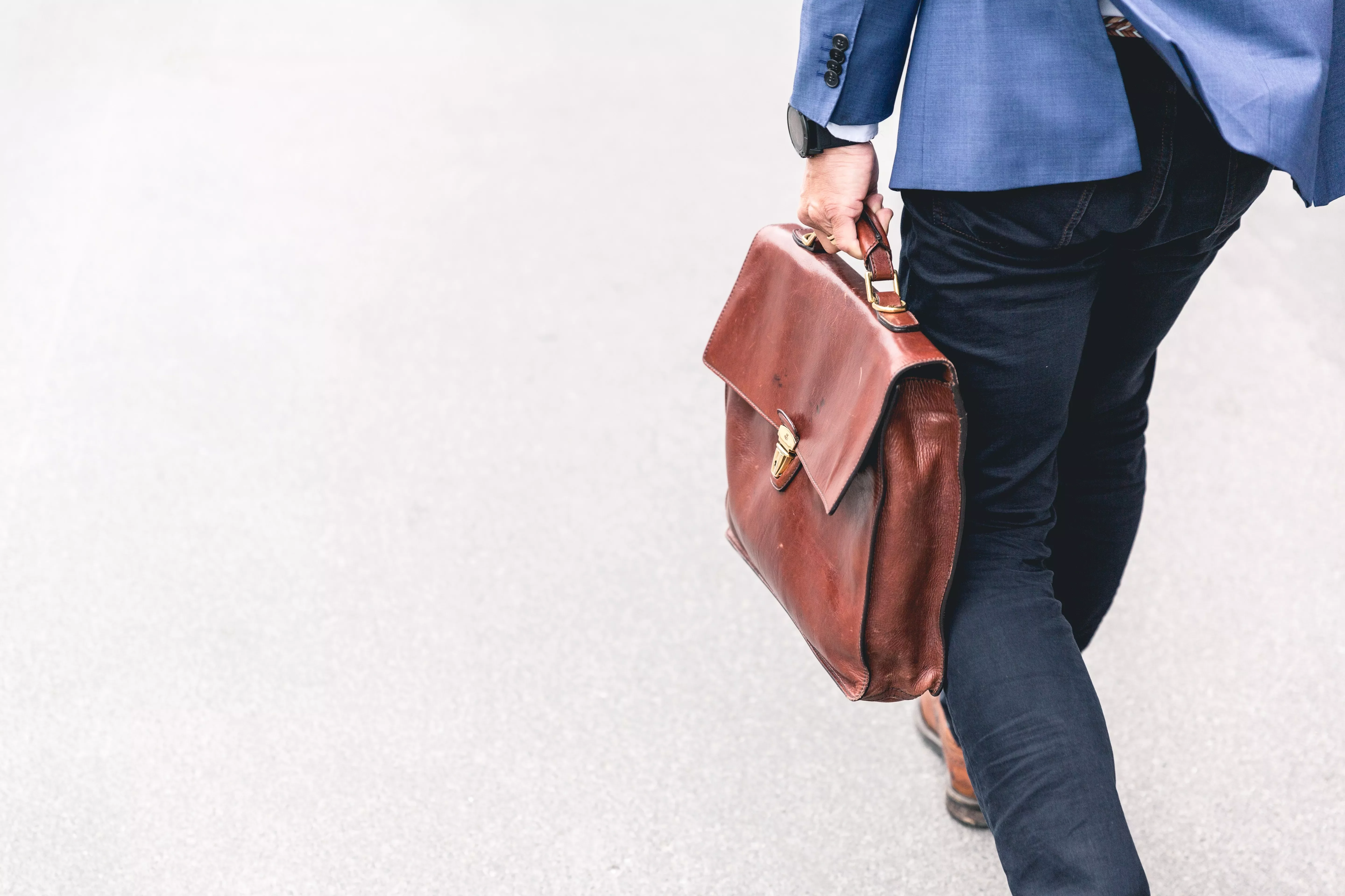 A person in a blue jacket walks with a brown briefcase.