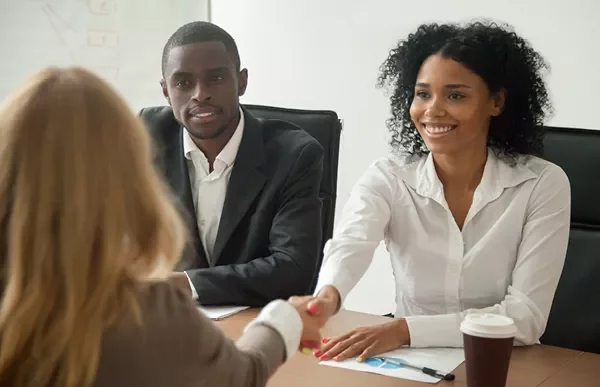 Two people at a business meeting shaking hands with another person.